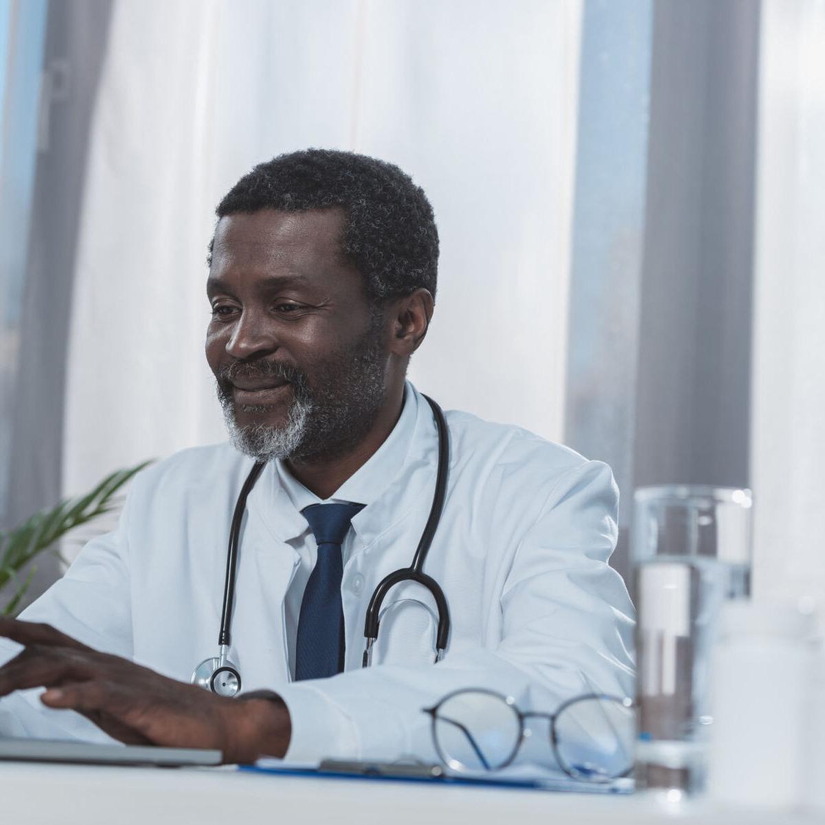 smiling african american doctor working with laptop in clinic