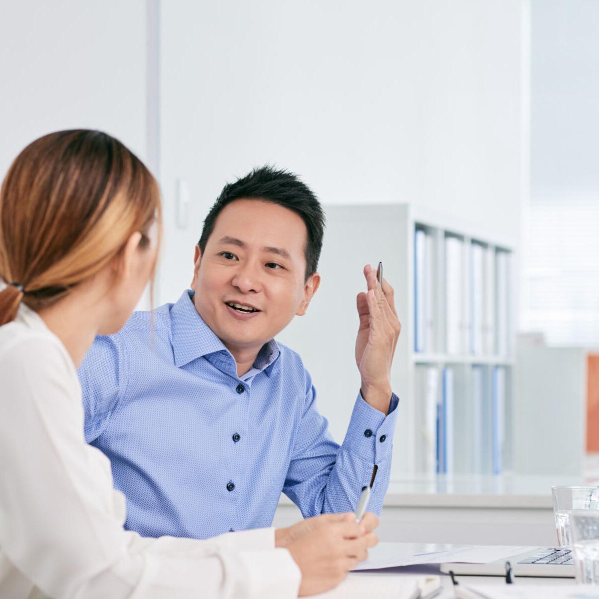 Cheerful Asian businessman talking to female coworker in office